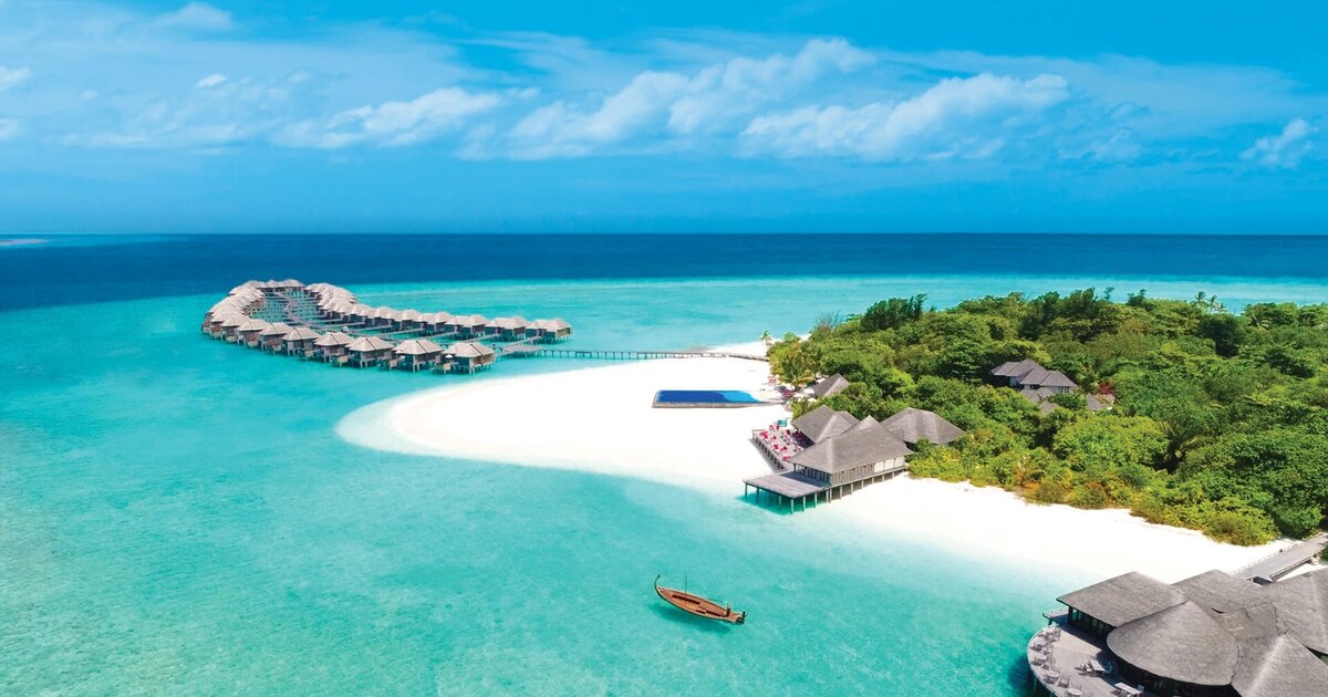 Aerial view of luxury wellness retreat in the Maldives — overwater villas, white sand beach and turquoise lagoon