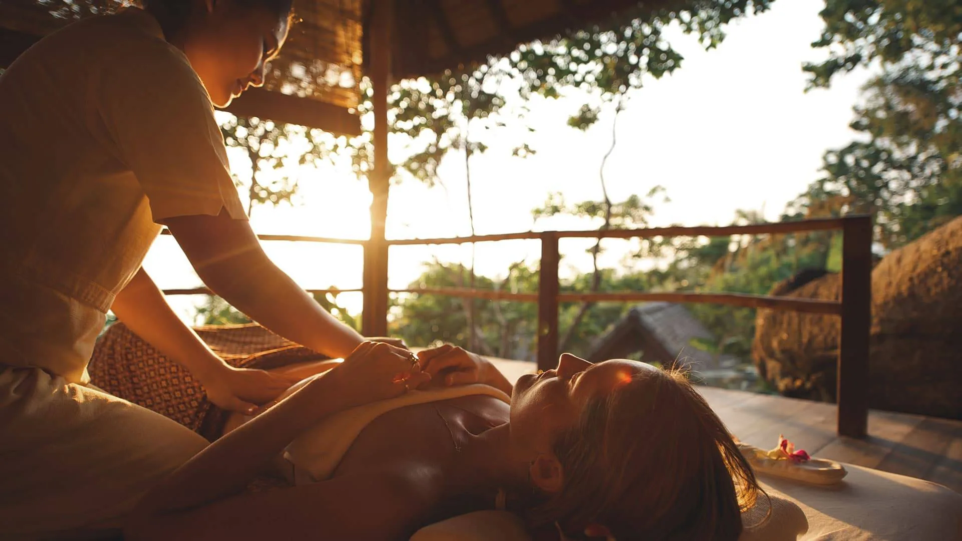 Holistic massage treatment at an open-air pavilion at Kamalaya Koh Samui with golden sunset light filtering through the jungle
