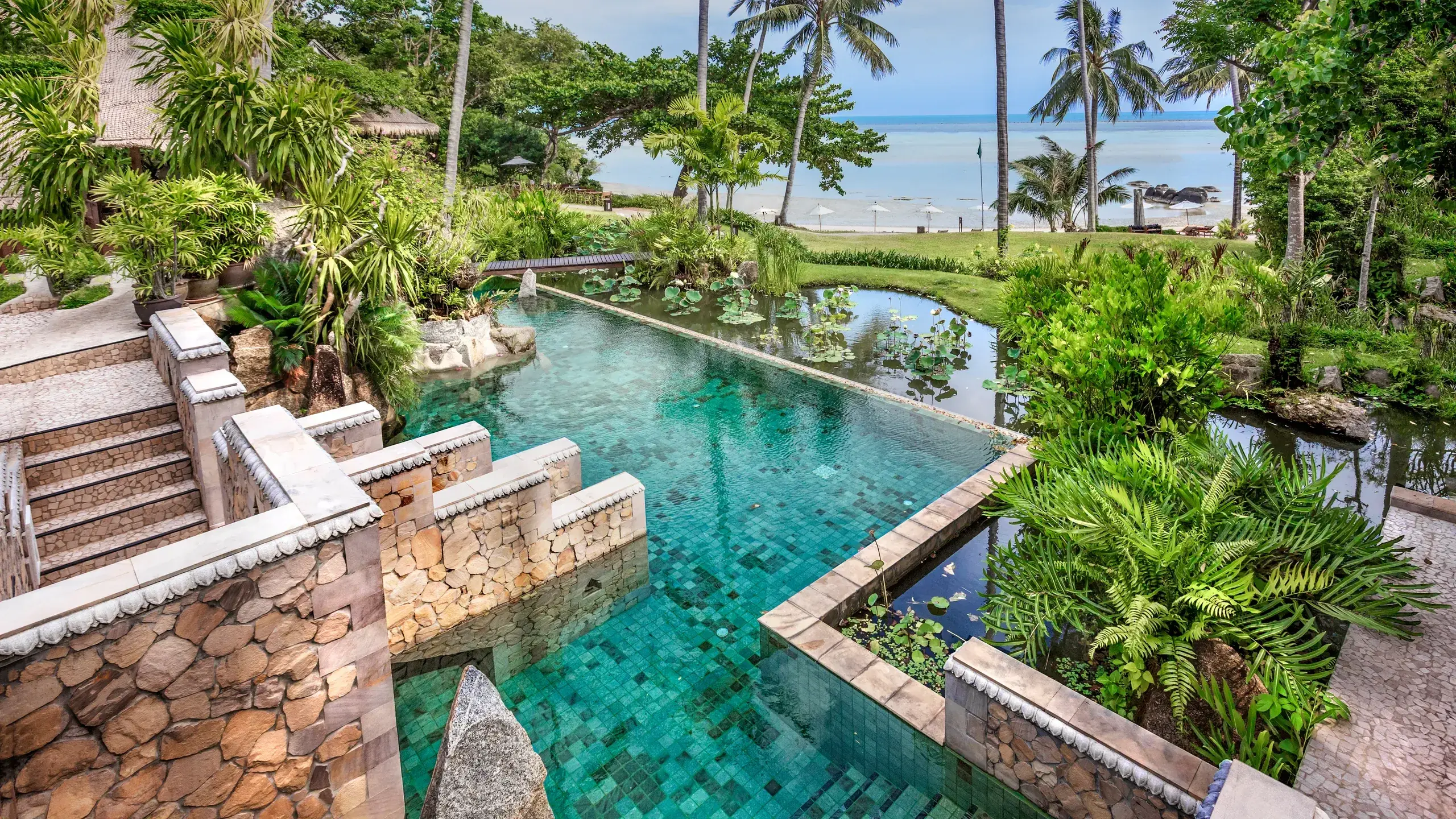 Stone infinity pool surrounded by lotus ponds and tropical gardens at Kamalaya Koh Samui with ocean in the background